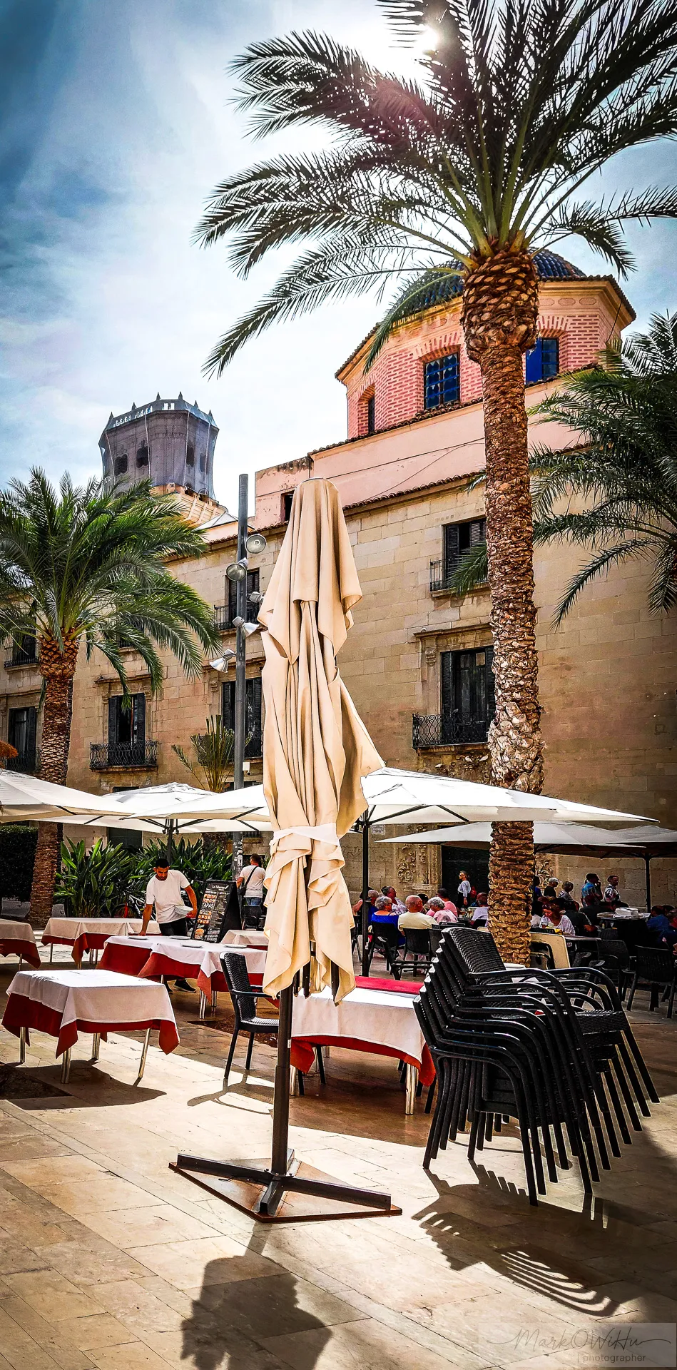 Sunlit square with palm tree and café terrace under blue sky | Foto Walk 2026 Alicante | MarkOWiHu Photographer
