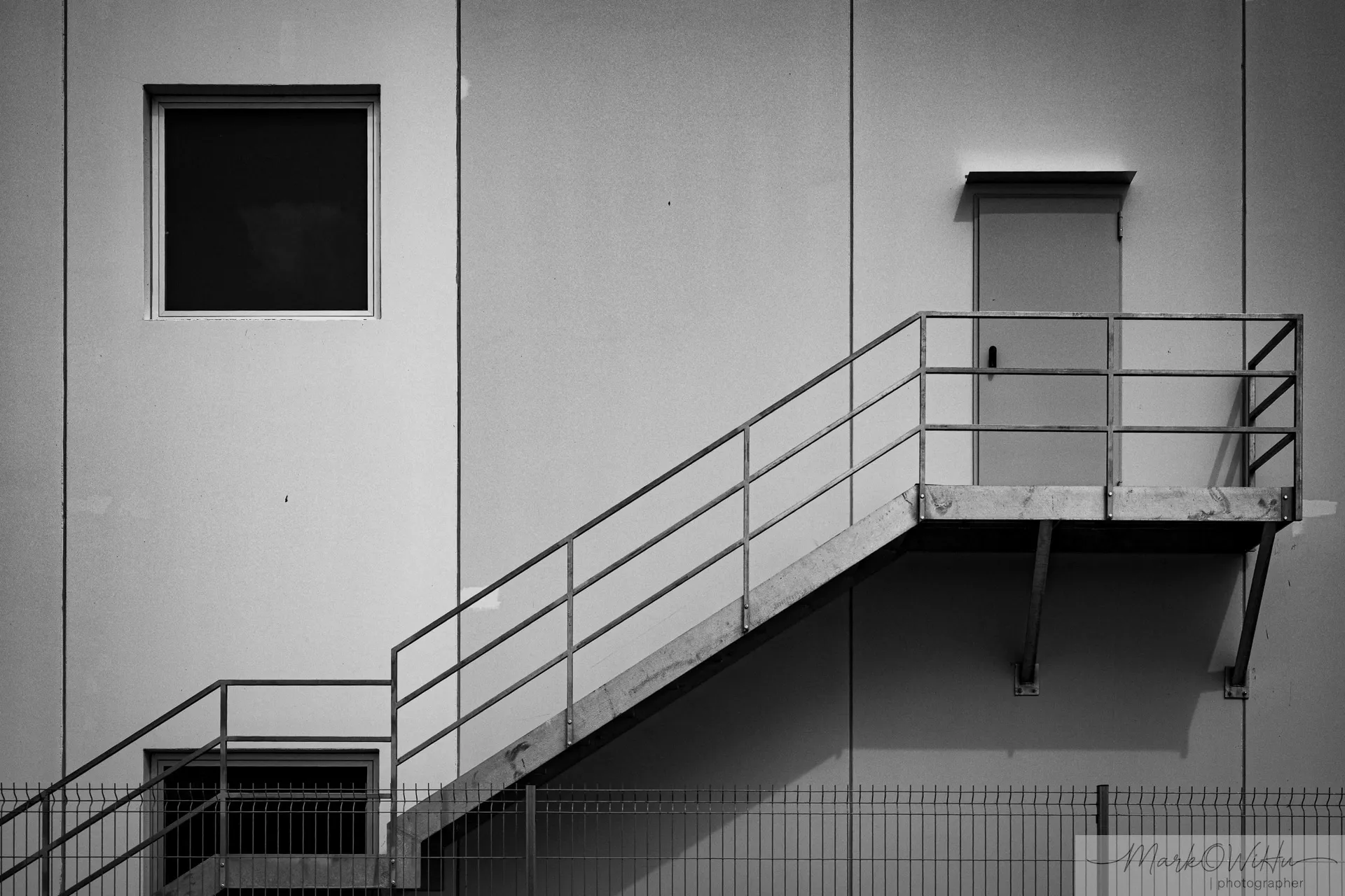 Minimalist black and white architectural detail of a metal staircase against a concrete industrial building facade