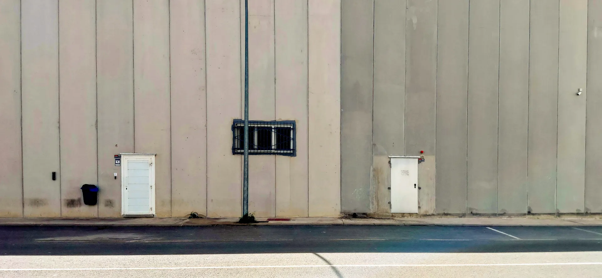 Minimalist urban texture showing a vast blank factory wall with two small white doors in Sol LeWitt style