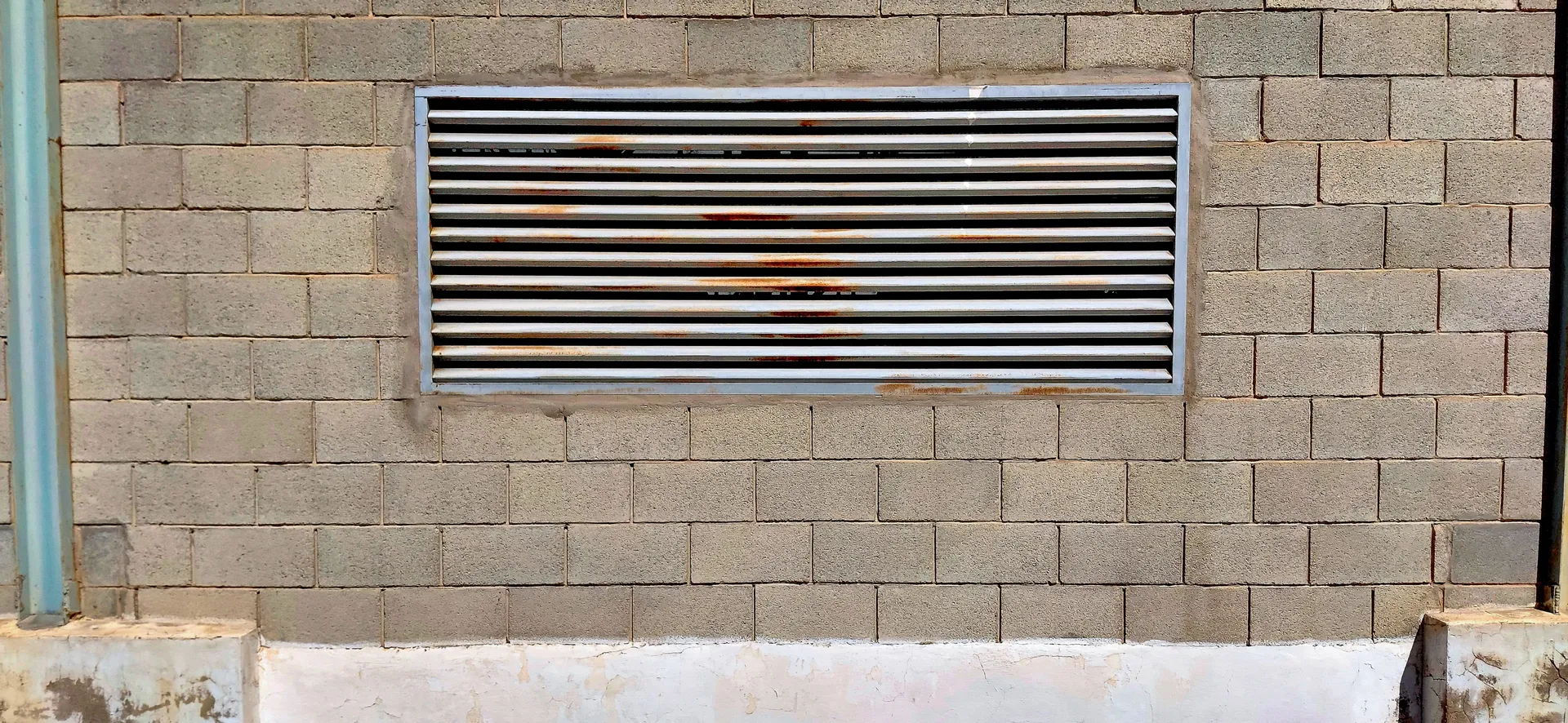 Industrial minimalism featuring a stainless steel slatted air vent grid on a grey cinderblock wall