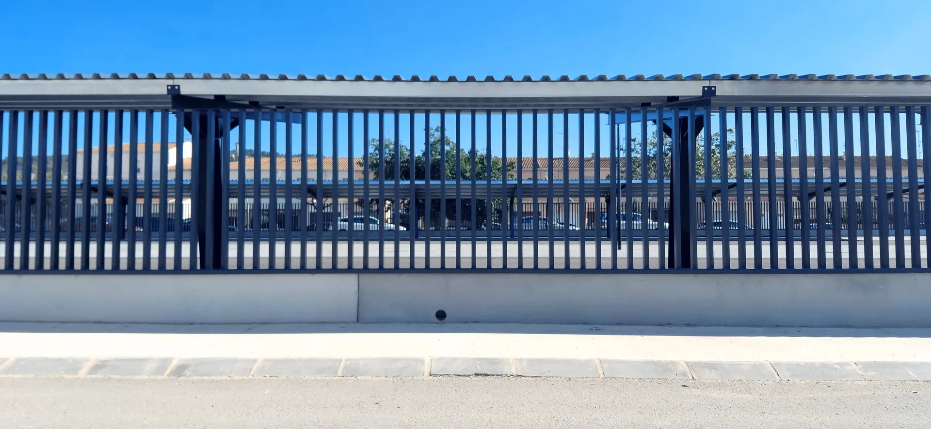 Minimalist horizontal black slatted security fence against a clean white urban curb