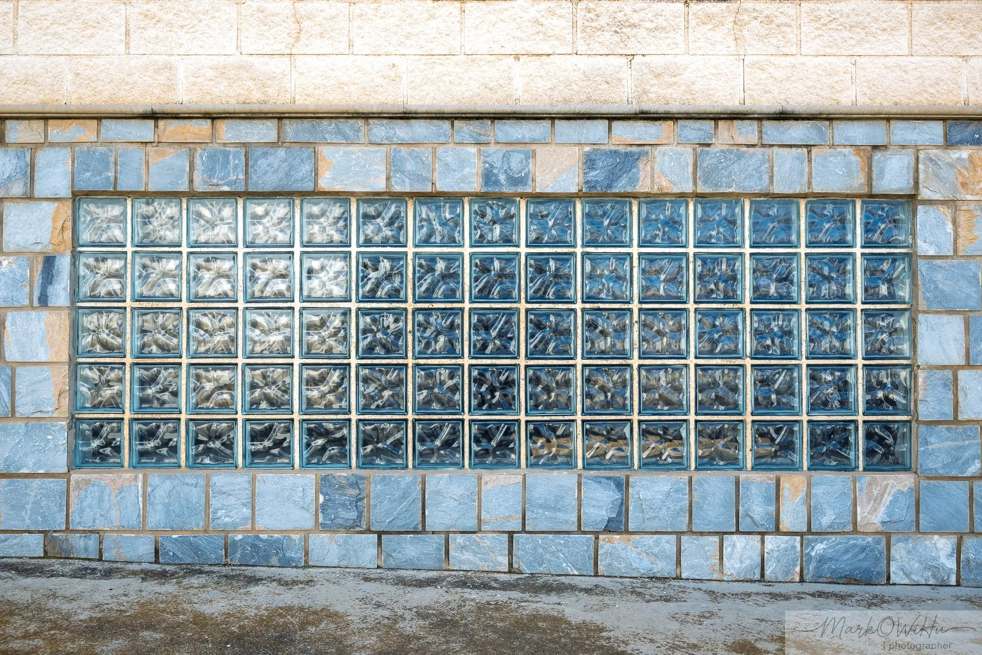 Industrial glass block window framed by blue tile border in a concrete wall