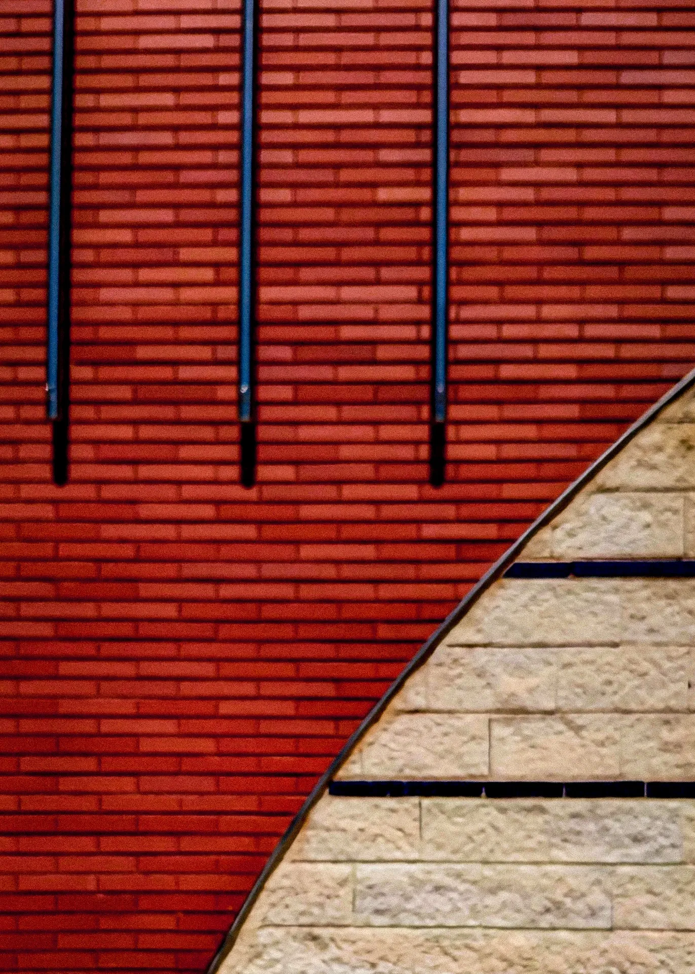 Color field composition of a red slatted industrial wall intersecting textured beige stone at a sharp diagonal
