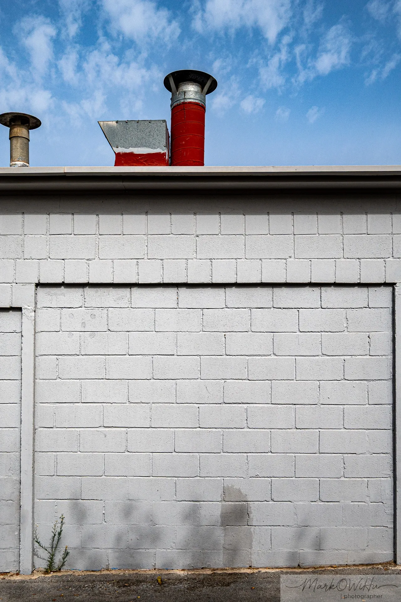 Hopper-esque minimalist composition of a red industrial chimney stack casting a sharp shadow on a white roof wall