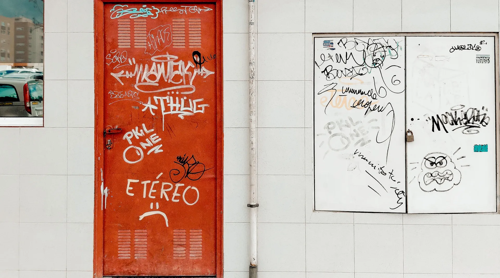 Urban wall texture study of a vibrant red metal door covered in white graffiti tags