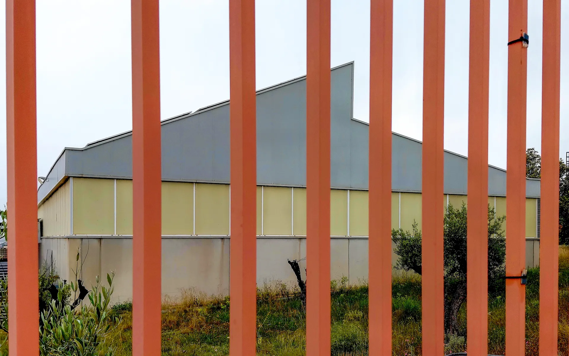 Industrial workplace fence with vertical orange slatted bars over grey building geometry