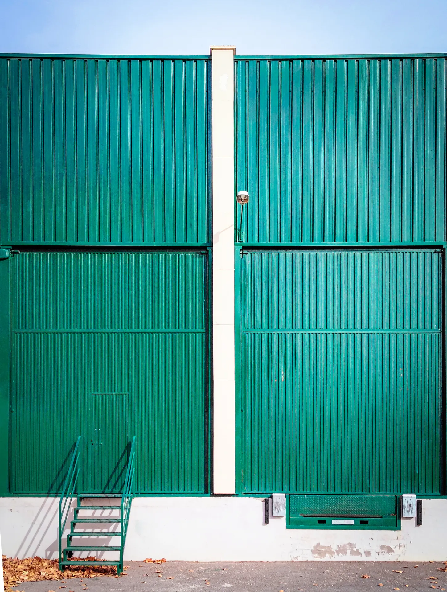 Vibrant green corrugated industrial door with a small ladder leaning against the wall