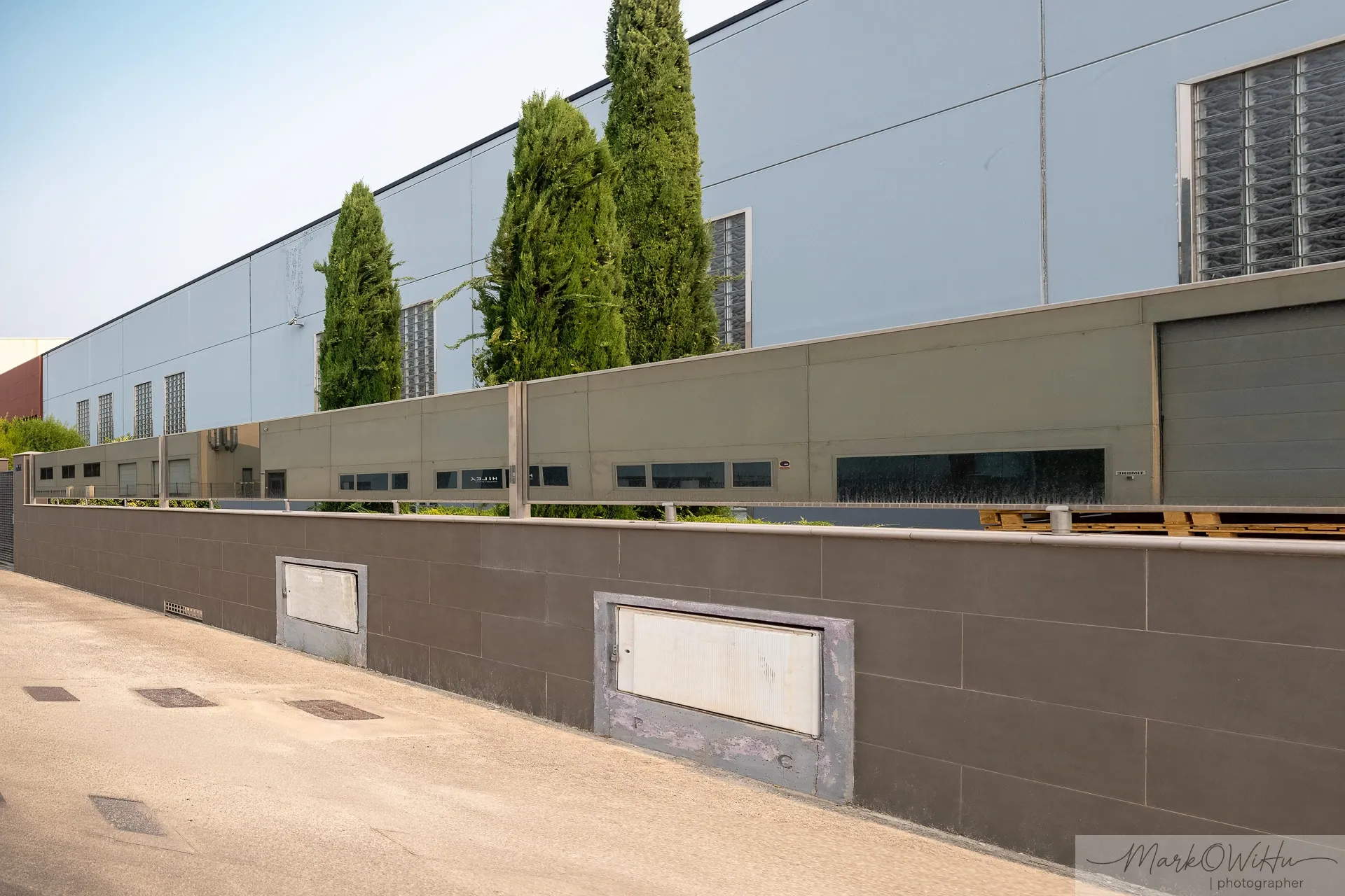 Long grey industrial factory building perspective lined with green cypress trees